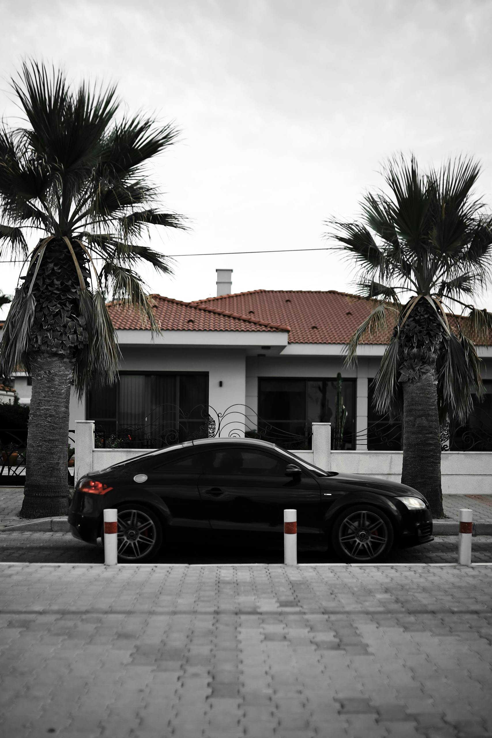 A sleek black car parked in front of a villa surrounded by palm trees in İzmir, Turkey.